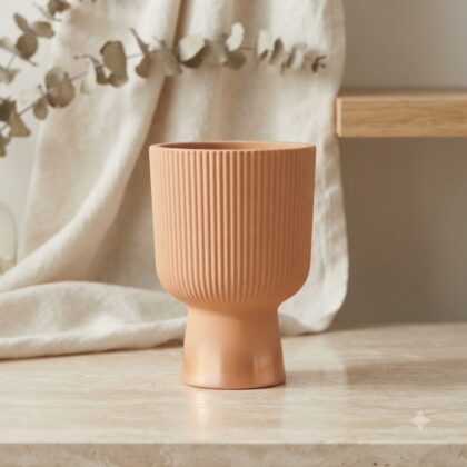Erika planter with a fluted texture on a pedestal base displayed on a countertop.