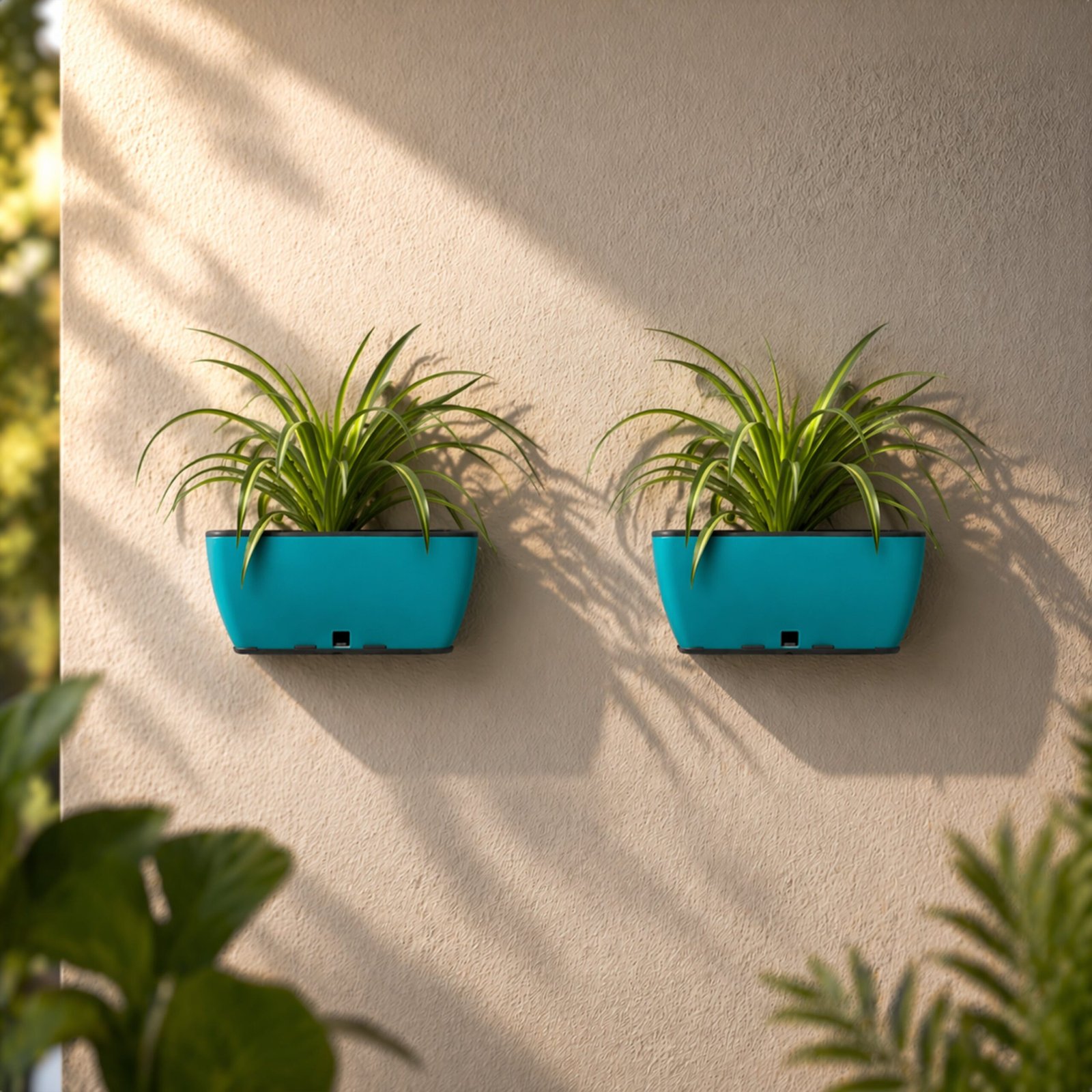 Two seagreen wall-mounted planters holding green plants mounted on a textured exterior wall.