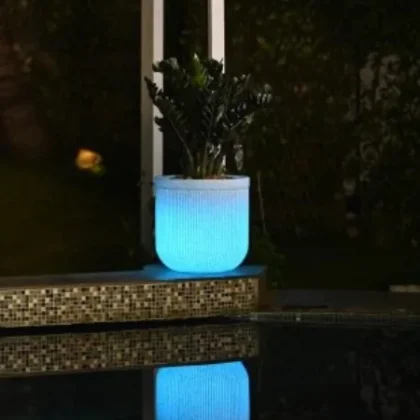 Illuminated white plant pot glowing with blue light beside a pool at night.