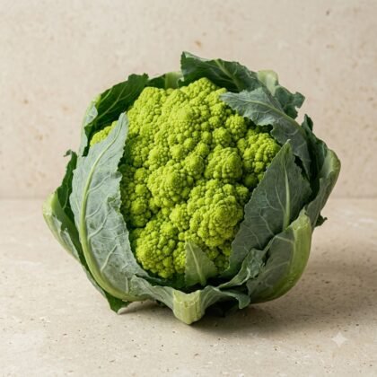A whole green romanesco broccoli with intricate fractal patterns, surrounded by outer leaves on a neutral surface.